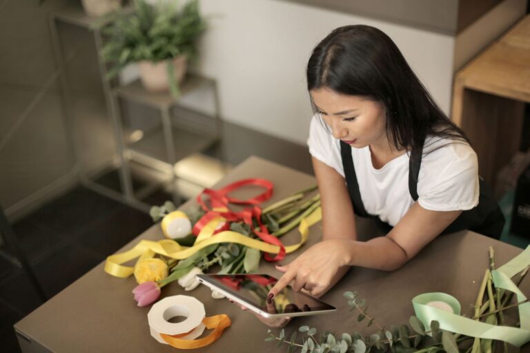 Florista usando um tablet no balcão da loja enquanto monta um arranjo, exemplo de pequena empresa usando tecnologia no dia a dia